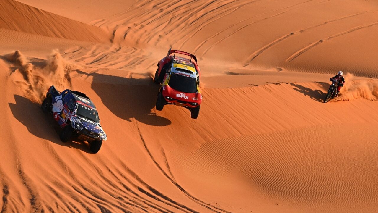 Sebastien Loeb (C) flies past biker Charlie Herbst and Overdrive Racing's Ronan Chabot on his way to victory in a marathon stage 6 of the Dakar Rally