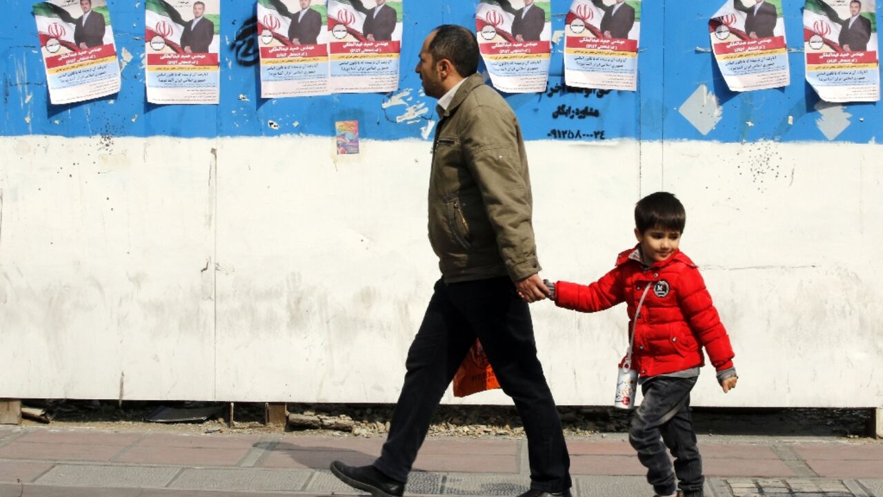 A man and a child walk past electoral campaign posters bearing portraits of a parliamentary candidate during the first day of election campaigning in Tehran