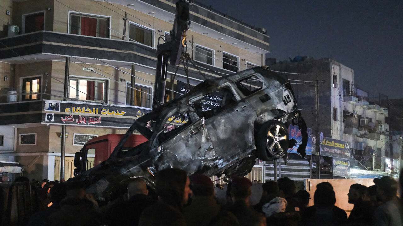 People watch as a vehicle that was hit by a drone strike, reportedly killing three people including two leaders of a pro-Iran group, is carried away in Baghdad on Feb. 7, 2024. 