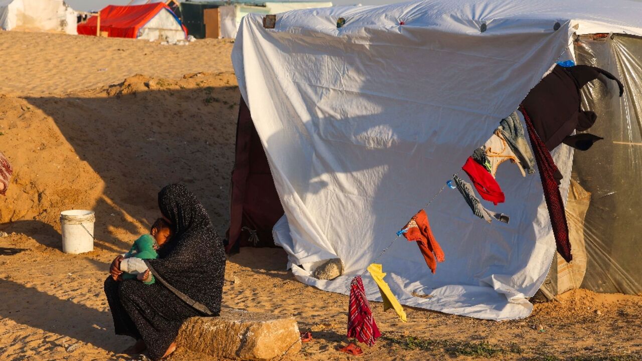 A displaced Palestinian woman cuddles her baby near her tent at a camp in Rafah on March 11, 2024