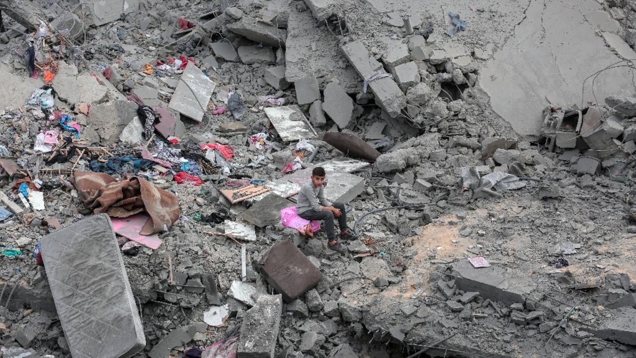 A boy sits among the rubble and scattered belongings of a home was destroyed in an Israeli strike in Deir el-Balah in the central Gaza Strip