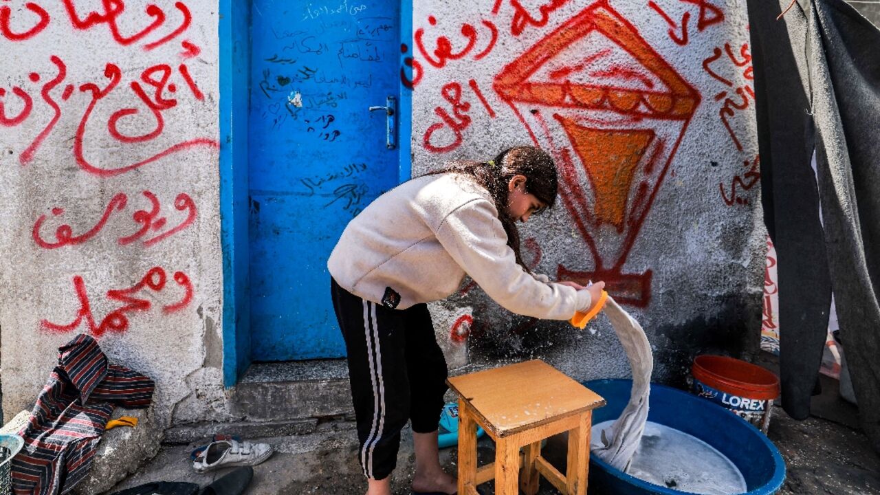 A girl washes clothes by hand at a camp for displaced Palestinians erected in a school run by the United Nations Relief and Works Agency for Palestine Refugees (UNRWA) in Rafah in the southern Gaza Strip on March 13, 2024