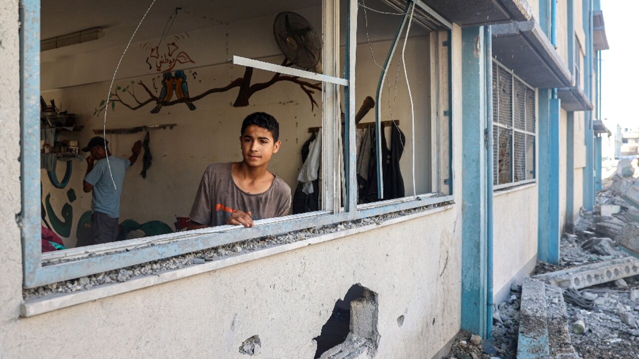 A Palestinian boy stands by a shattered window at a UN school sheltering displaced people which was damaged during Israeli bombardment in Khan Yunis, southern Gaza