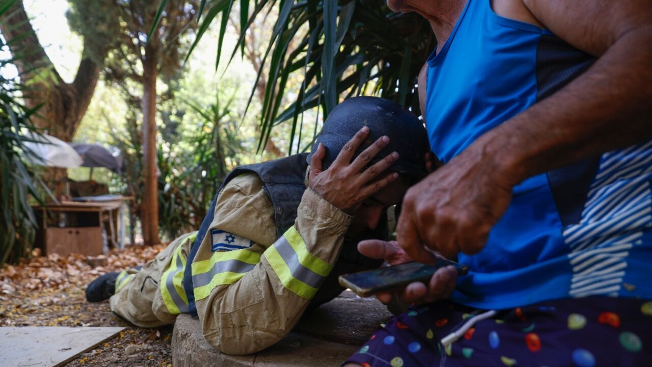 An Israeli firefighter and a resident take cover as sirens sound to warn of rockets launched from southern Lebanon, amid near-daily cross-border clashes