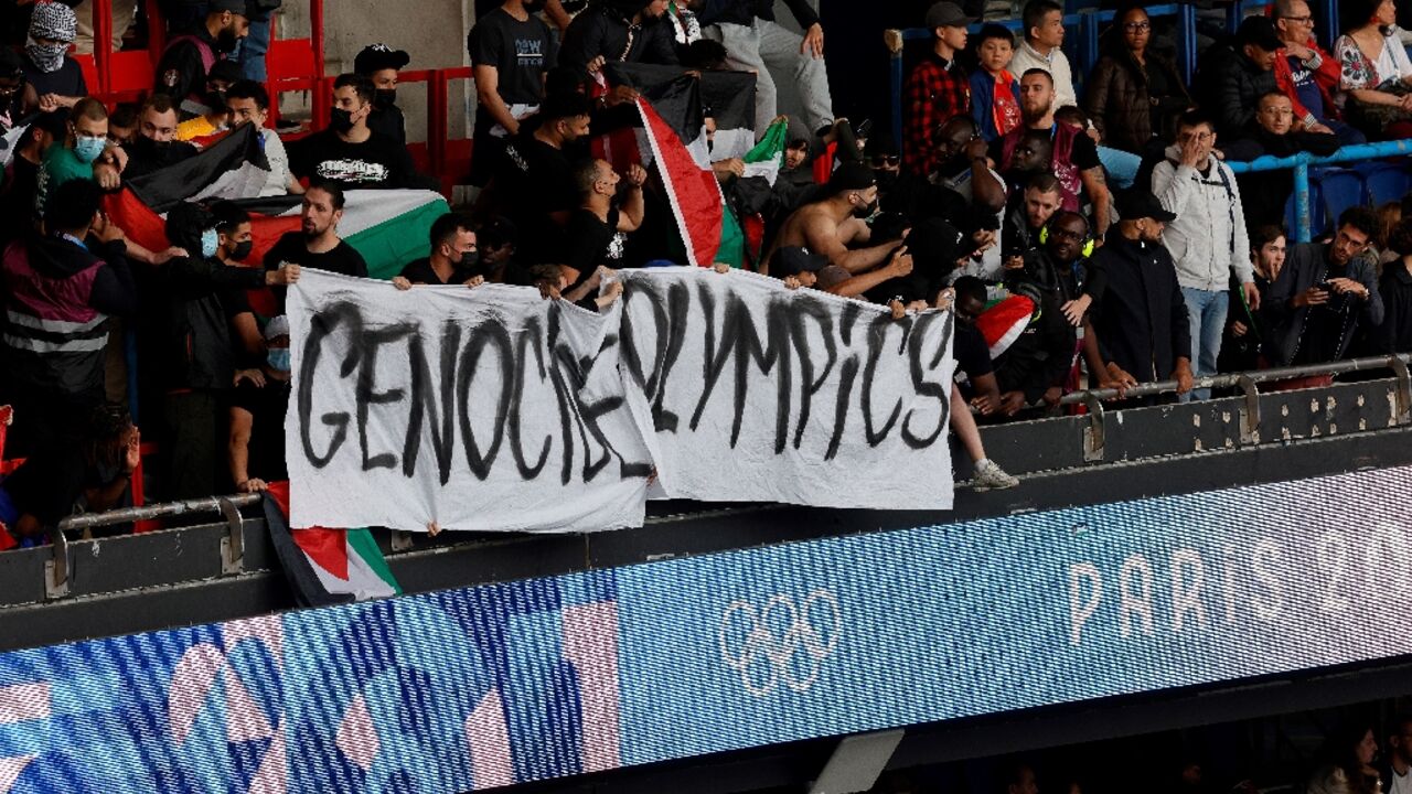 Supporters hold a banner reading "Genocide Olympics" and wave Palestinian flags at the Olympic football match between Israel and Paraguay on Saturday