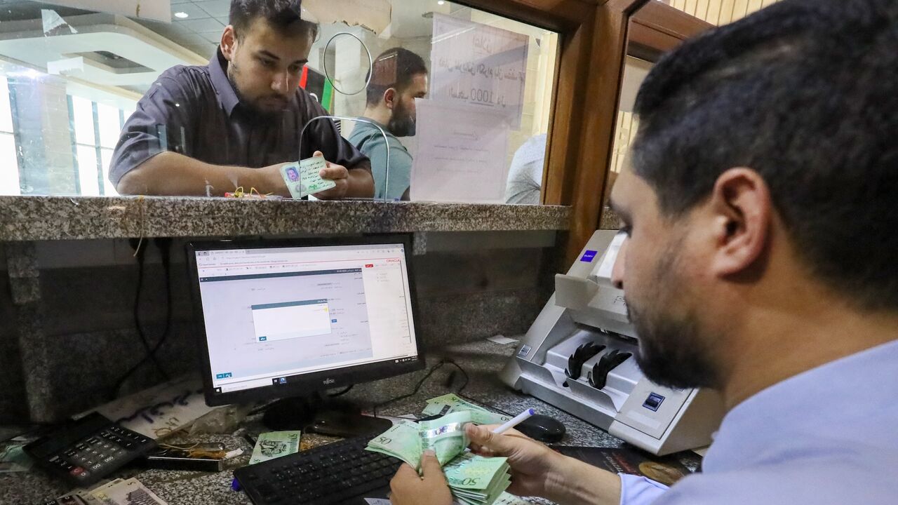 A bank teller counts money as a customer looks on at a bank in Libya's western coastal city of Misrata on Aug. 25, 2024.