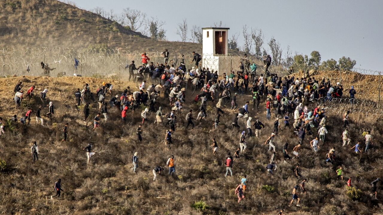 Migrants storm a barbed-wire fence as they attempt to cross the land border with Spain's African enclave of Ceuta near Fnideq in northern Morocco