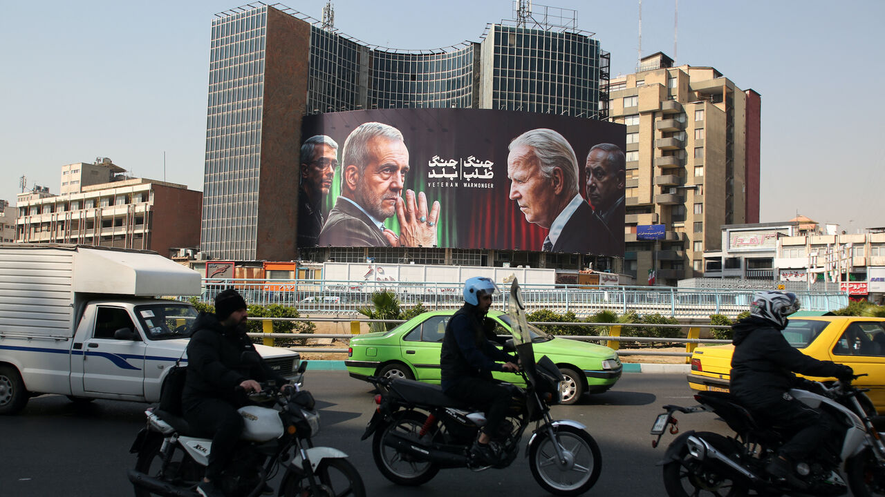 Commuters drive past a billboard bearing pictures of Iran's President Masoud Pezeshkian (2-L), armed forces chief of staff Major General Mohammad Bagheri (L) US President Joe Biden (2-R) and Israeli Prime Minister Benjamin Netanyahu (R) in Vali-Asr square in Tehran on Oct. 27, 2024.