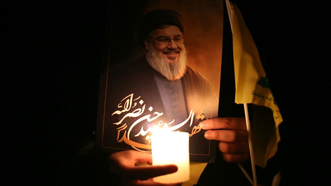 A mourner carries a candle and a portrait of slain Hezbollah chief Hassan Nasrallah during a vigil at the site where he was killed