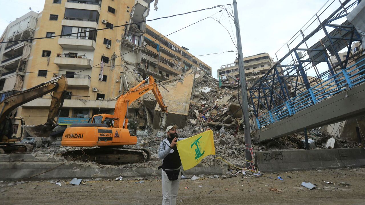 A Hezbollah supporter holds up the yellow flag of the Lebanese militant group in front destruction in Beirut's southern suburbs as people rushed back to check their homes on November 27, 2024, after a ceasefire between Israel and Hezbollah took effect. 