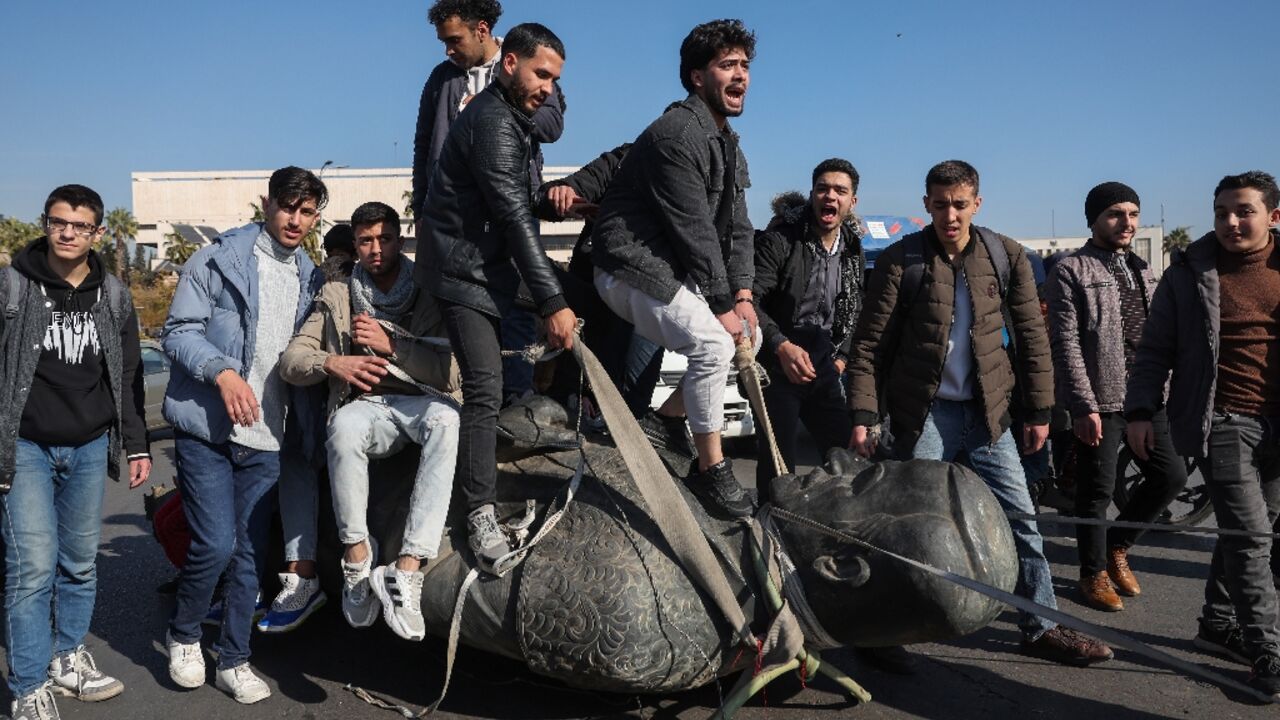 Students stand on the toppled statue of late president Hafez al-Assad during a rally near Damascus University