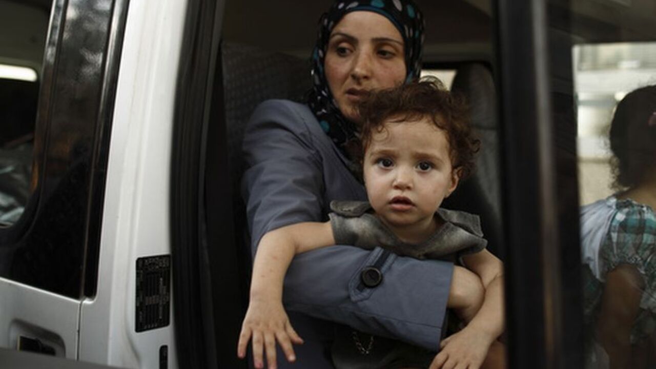 A Syrian woman carries her daughter as their family are about to cross back into Syria at the Turkish Cilvegozu border, opposite the Syrian commercial crossing point Bab al-Hawa, in Reyhanli, Hatay province, July 25, 2012. The Syrian family of five travelling back to Syria said they prefer risking death in their home country rather than stay in Turkey. Turkey has closed its border gates with Syria to commercial traffic due to worsening security conditions but will keep them open for refugees fleeing the Syr