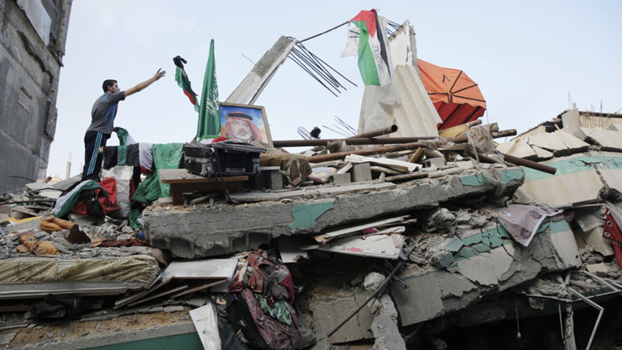 A Palestinian man throws a flag atop the rubble of the home of Hamas Gaza leader Ismail Haniyeh, which Gaza's interior ministry said was hit by a missile fired by Israeli aircraft before dawn on Tuesday, causing damage but no casualties, in Gaza City July 29, 2014. Israel's military pounded targets in the Gaza Strip on Tuesday after Prime Minister Benjamin Netanyahu said his country needed to be prepared for a long conflict in the Palestinian enclave, squashing any hopes of a swift end to 22 days of fightin