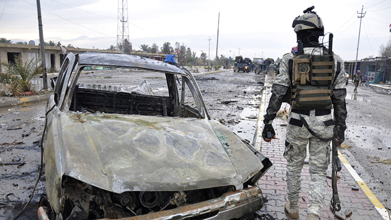A member of the Iraqi security forces walks past a destroyed vehicle belonging to Islamic State militants during an intensive security deployment on the outskirts of Samarra December 14, 2014. Picture taken December 14, 2014. REUTERS/Stringer (IRAQ - Tags: CIVIL UNREST POLITICS MILITARY) - RTR4I0GG