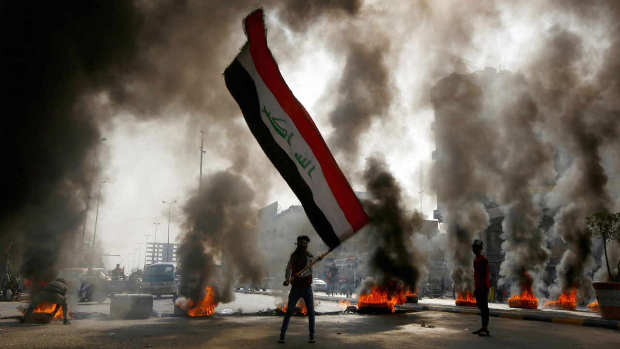 A protester holds an Iraqi flag amid a cloud of smoke from burning tires during ongoing anti-government protests in Najaf, Iraq November 26, 2019. REUTERS/Alaa al-Marjani - RC2ZID9MARY6