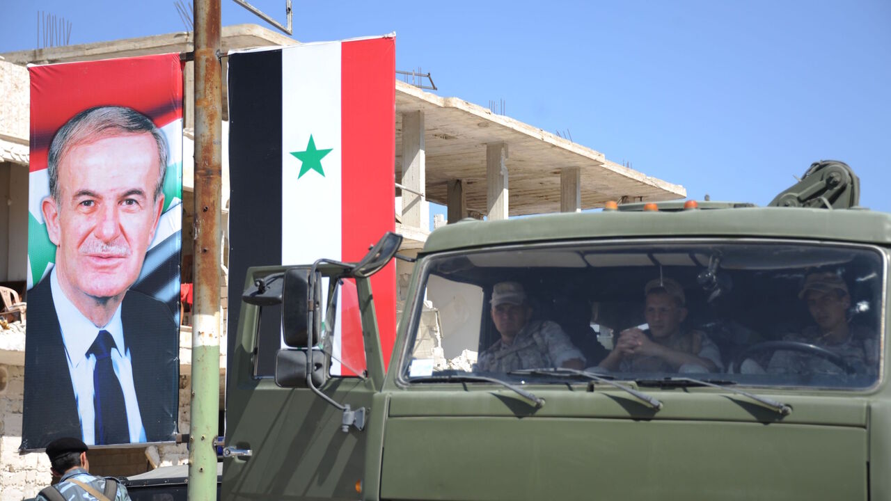Russian soldiers sit in their vehicle next to a portrait of late Syrian president Hafez al-Assad in Khan Sheikhun in the southern countryside of the Idlib province on September 25, 2019. - With military backing from Russia, President Bashar al-Assad's forces have retaken large parts of Syria from rebels and jihadists since 2015, and now control around 60 percent of the country. Russia often refers to troops it deployed in Syria as military "advisers" even though its forces and warplanes are also directly in
