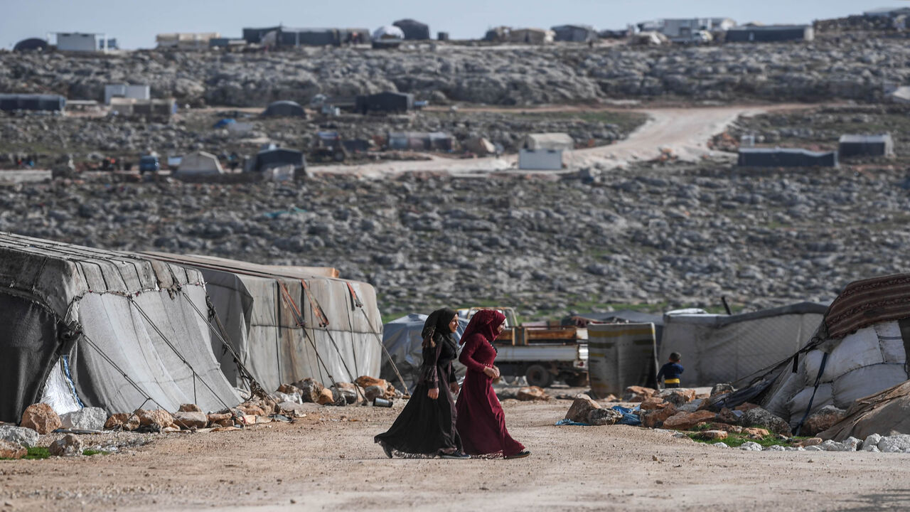 TOPSHOT - Displaced Syrian women walk at a camp in Kafr Lusin village on the border with Turkey in Syria's northwestern province of Idlib, on March 10, 2020. - When protesters in March 2011 demanded their rights and regime change, they likely never imagined it would trigger a reaction that has led to the 21st century's biggest war. Nine years on, President Bashar al-Assad is still in power and there to stay, more than 380,000 people have died, dozens of towns and cities razed to the ground and half of the c