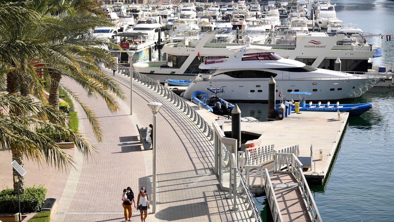 Women wearing protective masks walk at the promenade of Dubai Marina on May 5, 2020, after authorities of the United Arab Emirates started to ease a national lockdown put in place to curb the spread of COVID-19 coronavirus. - In Dubai's ritzy Marina district, white yachts are tethered to docks, standing idle -- like many companies behind a luxury lifestyle industry battered by the coronavirus crisis. The boardwalks that snake around the precinct's artificial bays and canals, once packed with tourists, mostl