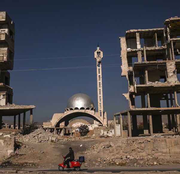 A man rides his scooter past a destroyed mosque and apartment buildings in Harasta, near the Syrian capital, Damascus, on Dec. 19, 2024. 