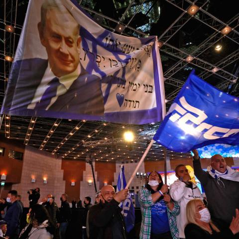 Likud party supporters wave flags bearing the party's leader, Prime Minister Benjamin Netanyahu, as they react at their party campaign headquarters in Jerusalem on March 23, 2021