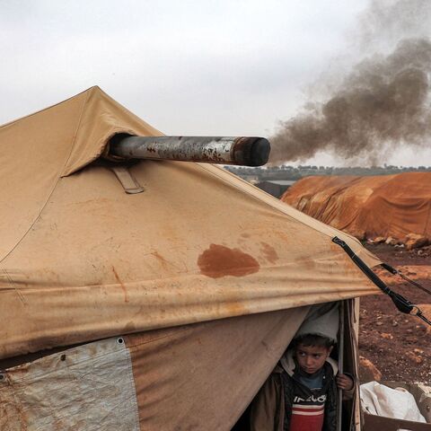 Smoke from an indoor bonfire exits from the chimney of the tent of Umm Raed at a camp for the displaced.