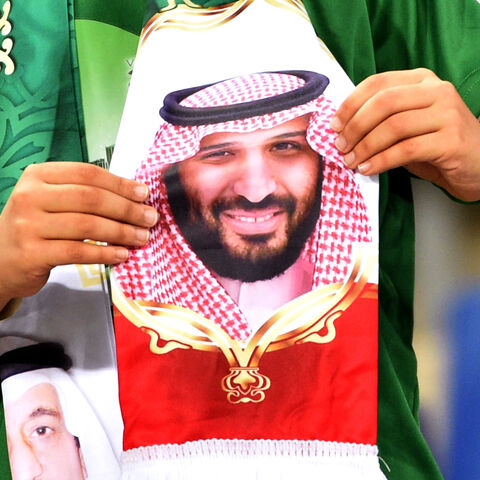 A Saudi fan holds a scarf with portraits of King Salman (L) and his son, Crown Prince Mohammed bin Salman.