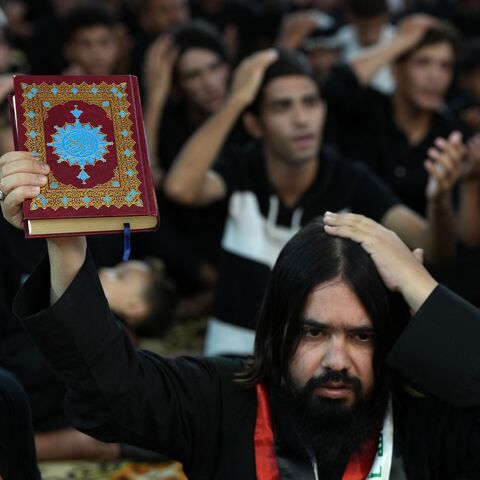 A Shiite Muslim man raises a Koran as he takes part in a mourning ritual in the city of Nasiriyah in Iraq's southern Dhi Qar province eraly on July 22, 2023, during the Muslim month of Muharram in the lead-up to Ashura. Ashura is a 10-day mourning period commemorating the seventh century killing of Prophet Mohammed's grandson Imam Hussein. (Photo by Asaad NIAZI / AFP) (Photo by ASAAD NIAZI/AFP via Getty Images)
