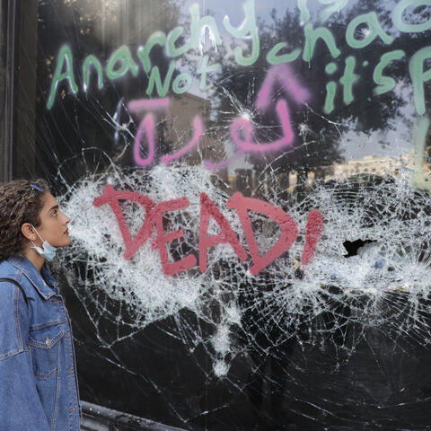 A Lebanese woman looks at graffiti on a smashed glass facade in the heart of the capital Beirut on October 25, 2019 as anti-corruption demonstrators cut off major roads across the country for a ninth day, pledging to carry on with their protests despite the president offering to meet their representatives. - The entire political class has been targeted in days of unprecedented street demos that have dominated city centres and closed banks, schools and universities across Lebanon. (Photo by ANWAR AMRO / AFP)