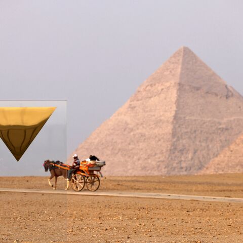 Tourists ride in a horse-drawn carriage near the art installation "Temple" by French artist Stephan Breuer and the Pyramid of Menkaure or Menkheres (front) and the Pyramd of Khafre or Chephren (behind) during the third edition of the "Forever is Now" art exhibition by Art d'Egypte at the Giza pyramids necropolis on October 28, 2023. (Photo by Khaled DESOUKI / AFP) / RESTRICTED TO EDITORIAL USE - MANDATORY MENTION OF THE ARTIST UPON PUBLICATION - TO ILLUSTRATE THE EVENT AS SPECIFIED IN THE CAPTION (Photo by 