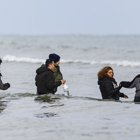 TOPSHOT - Migrants walk in the sea to board a smuggler's boat in an attempt to cross the English Channel, on the beach of Gravelines, near Dunkirk, northern France on April 26, 2024. Five migrants, including a seven-year-old girl, died on April 23, 2024 trying to cross the Channel from France to Britain, local authorities said, just hours after Britain passed a controversial bill to deport asylum seekers to Rwanda. (Photo by Sameer Al-DOUMY / AFP) (Photo by SAMEER AL-DOUMY/AFP via Getty Images)