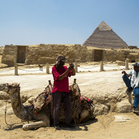 A man checks his mobile phone standing next to his camel while waiting for tourists at the Giza Pyramids Necropolis on the outskirts of Giza on April 30, 2024. (Photo by Jewel SAMAD / AFP) (Photo by JEWEL SAMAD/AFP via Getty Images)