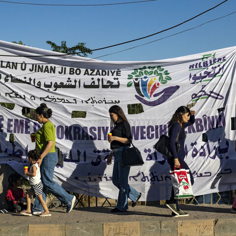 Syrian Kurdish women walk past an election campaign banner in the northeastern Syrian city of Qamishli on June 6, 2024. 