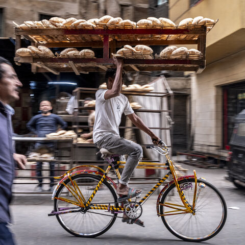 TOPSHOT - A deliveryman balances a tray of freshly baked bread while riding his bicycle along the al-Darb al-Ahmar district in the old quarters of Cairo on March 6, 2024. (Photo by Amir MAKAR / AFP) (Photo by AMIR MAKAR/AFP via Getty Images)