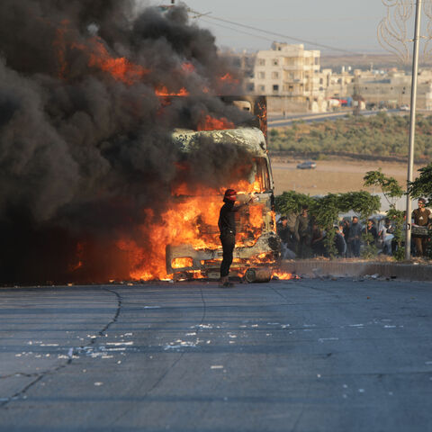 A protester stands in front a burning Turkish truck during protests against Turkey in al-Bab, in the northern Syrian opposition held region of Aleppo on July 1, 2024. A man was killed after and Turkish forces clashed in Syria's Ankara-controlled northwest , a war monitor said, in demonstrations sparked by violence against Syrians in Turkey a day earlier. (Photo by Bakr ALKASEM / AFP) (Photo by BAKR ALKASEM/AFP via Getty Images)