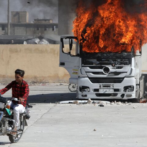 A man rides a motorcycle near a burning Turkish truck during protests against Turkey in al-Bab, in the northern Syrian opposition held region of Aleppo on July 1, 2024. 