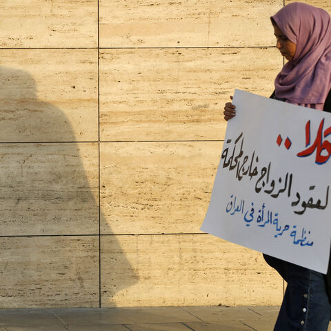 A woman walks holding a placard as activists demonstrate against female child marriages, in Tahrir Square in central Baghdad on July 28, 2024, amid parliamentary discussion over a proposed amendment to the Iraqi Personal Status Law. (Photo by AHMAD AL-RUBAYE / AFP) (Photo by AHMAD AL-RUBAYE/AFP via Getty Images)