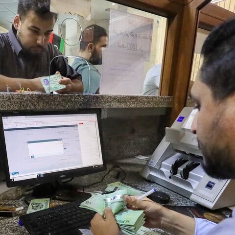 A bank teller counts money as a customer looks on at a bank in Libya's western coastal city of Misrata on Aug. 25, 2024.