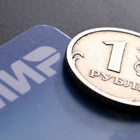 A photo taken on March 14, 2022, shows a Russian ruble coin and the Russian Mir payment system logo on a bank card in Moscow.