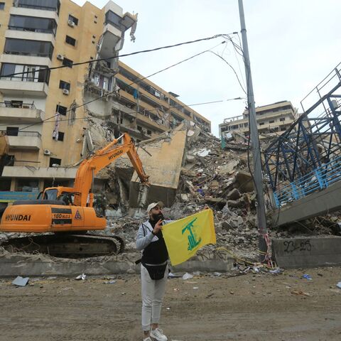 A Hezbollah supporter holds up the yellow flag of the Lebanese militant group in front destruction in Beirut's southern suburbs as people rushed back to check their homes on November 27, 2024, after a ceasefire between Israel and Hezbollah took effect. 