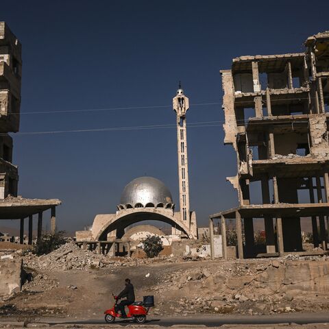 A man rides his scooter past a destroyed mosque and apartment buildings in Harasta, near the Syrian capital, Damascus, on Dec. 19, 2024. 