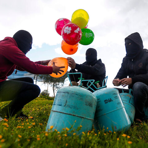 Masked Palestinians prepare to attach balloons to a gas canister before releasing it near Gaza's Bureij refugee camp, along the Israel-Gaza border fence, on February 10, 2020. (Photo by MAHMUD HAMS / AFP) (Photo by MAHMUD HAMS/AFP via Getty Images)