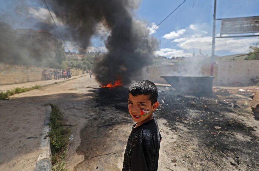 A Palestinian child stands in front of burning tyres in the refugee camp of Jenin in the occupied West Bank after an Israeli military raid on April 12, 2022