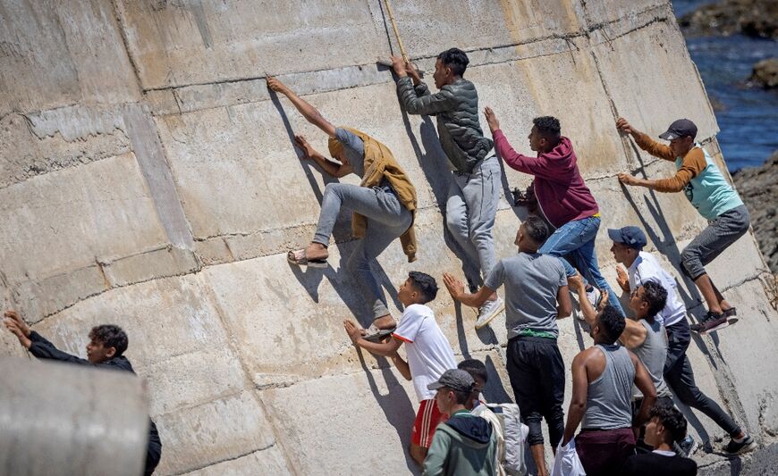 Migrants climb a sea wall in the northern town of Fnideq after attempting to cross the border from Morocco to Spain's North African enclave of Ceuta on May 19, 2021