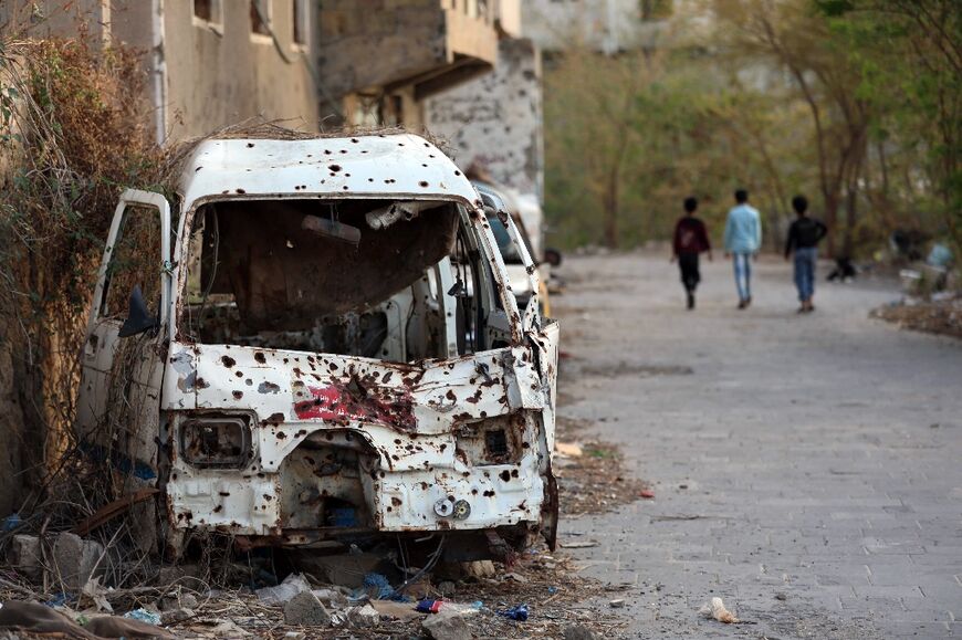 Boys walk past a shrapnel-ridden vehicle in Yemen's Taez, which is besieged by Iran-backed Huthi rebels
