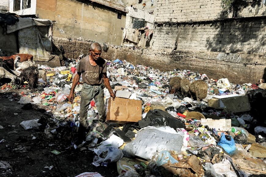 A man collects tin cans as sheep and goats graze on trash at a dump at the Sabra camp for Palestinian refugees in the southern suburbs of Lebanon's capital Beirut on September 9, 2022