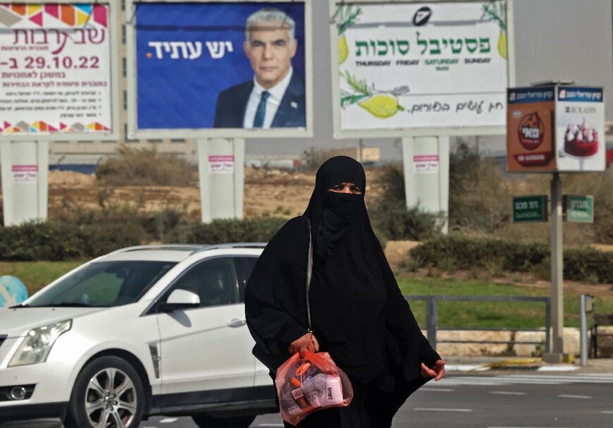 An Israeli Bedouin woman walks past an electoral banner for candidate and prime minister Yair Lapid, in the southern city of Beersheva