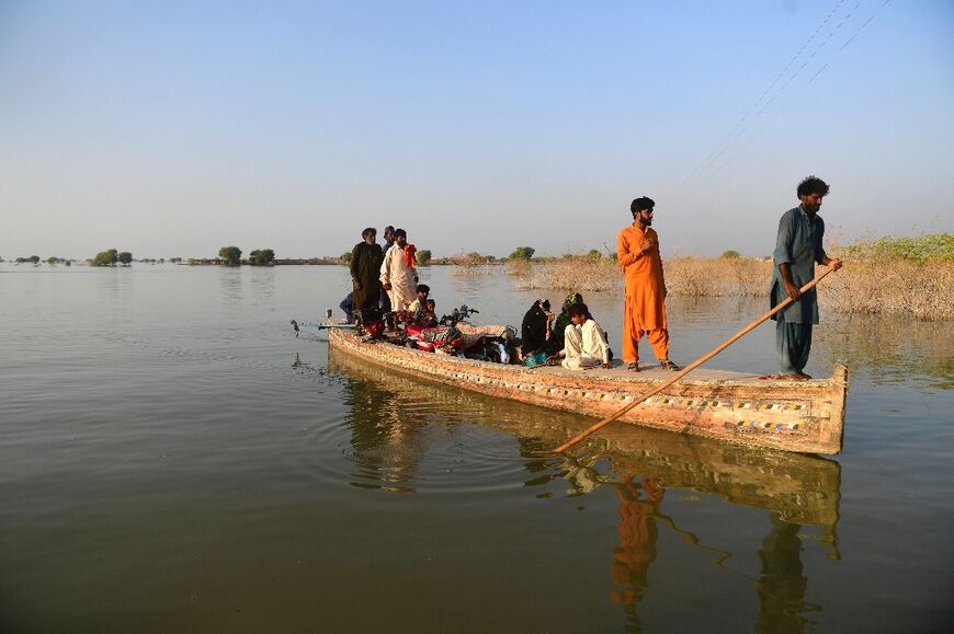 Internally displaced people use a boat to cross a flooded area at Dadu in Sindh province of Pakistan on October 27, 2022.
