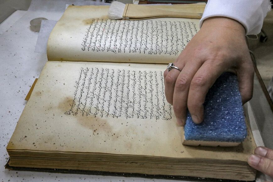 A conservator uses a sponge on a Persian-language manuscript undergoing restoration at the House of Manuscripts in Baghdad
