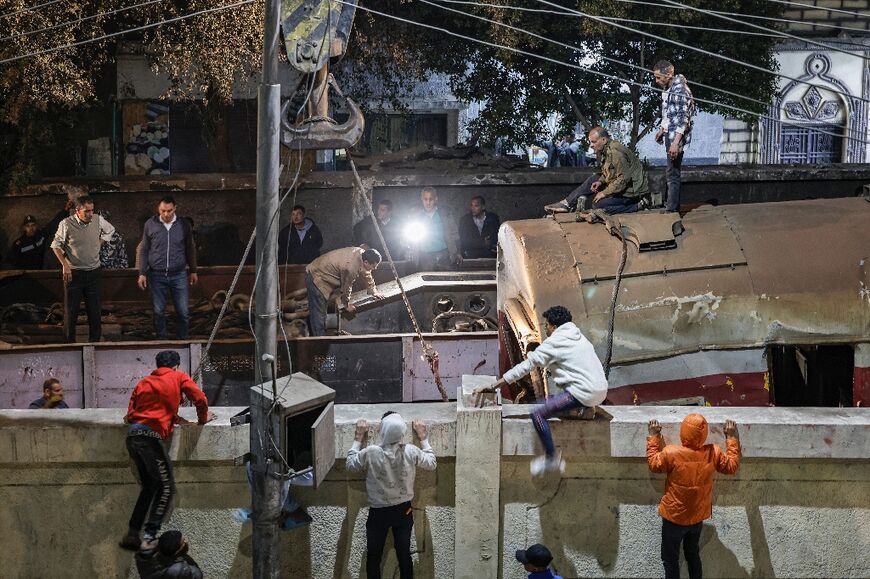 Youths climb a wall to watch as a crane lifts a derailed train carriage in the city of Qalyub north of Cairo
