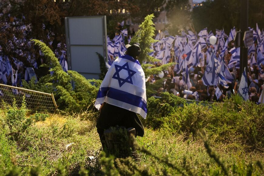 A pro-government protester draped in the Israeli flag attends a gathering near Israel's parliament in Jerusalem on April 27, 2023  